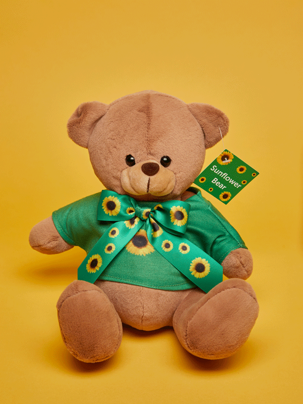 A brown teddy bear with a green Sunflower t-shirt and a bow tie sitting on a yellow background